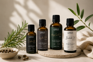 Vier Cobrend Naturals Pflegeöle in Braunglasflaschen auf Naturstein mit Rosmarin, Samen und natürlicher Stoffdekoration.